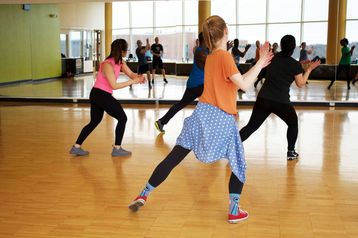 A dance class full of people practicing dance moves in front of a large mirror