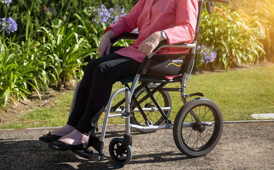 A woman shown in side profile from the shoulders down sitting in a wheelchair with a garden in the background