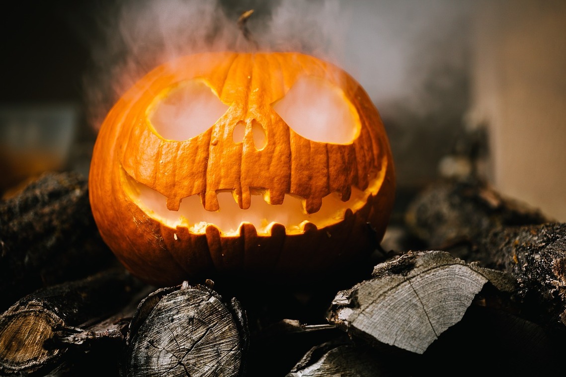 A skeleton style carved pumpkin with smoke coming out of the eyes on a bed of dark wood