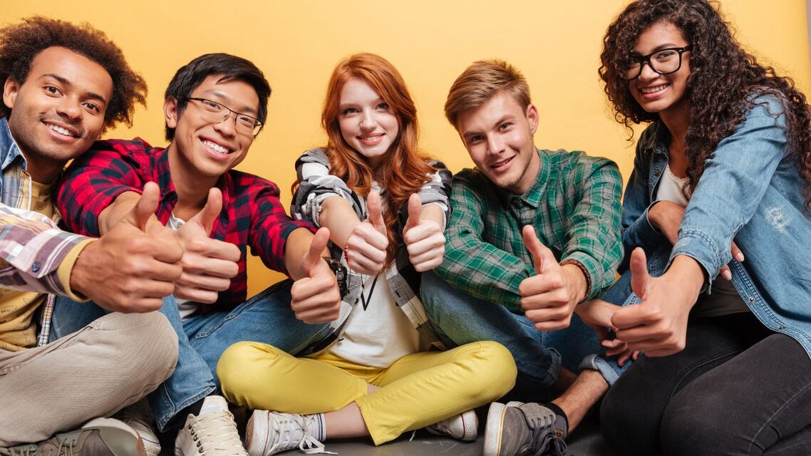 group of teenagers sitting in semi circle smiling and thumbs up