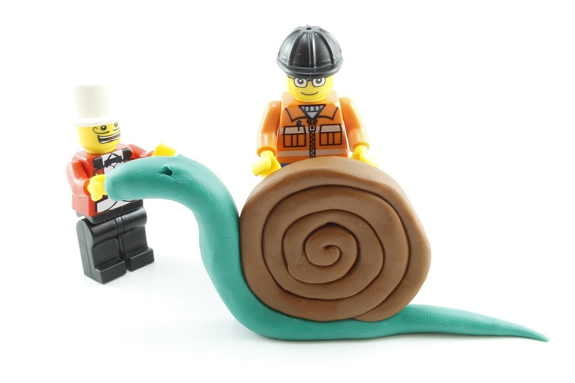 Two lego figures standing next to a plasticine green and brown snail